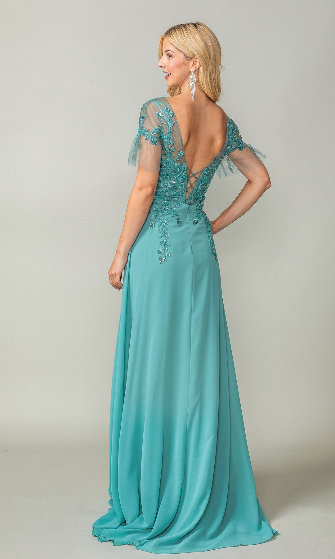 A woman faces away, wearing the Dancing Queen 4378 sheer short-sleeve prom dress—floor-length and teal, with floral embroidery, beaded accents, and a deep V-back.